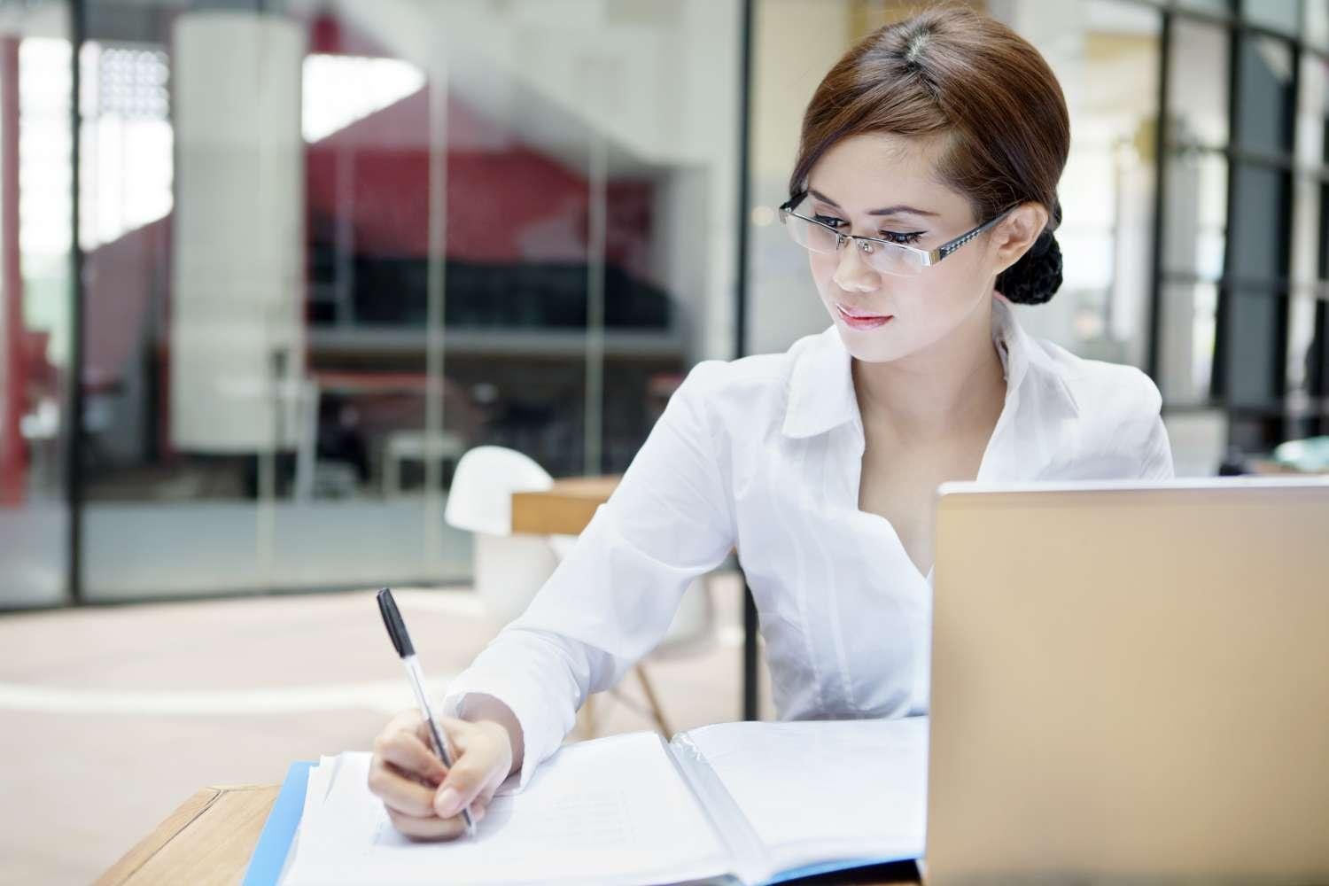 Businesswoman with Laptop writing on Document